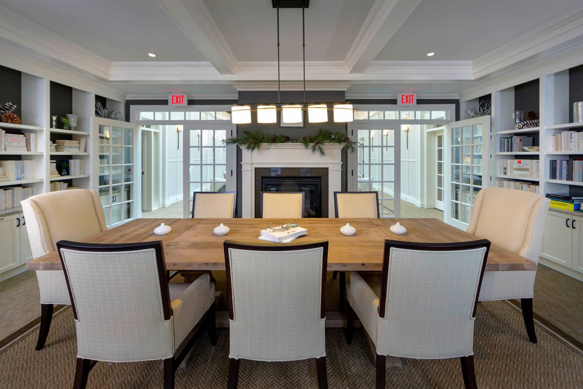 A stylish dining room with a wooden table and upholstered chairs, framed by large windows and a central fireplace.