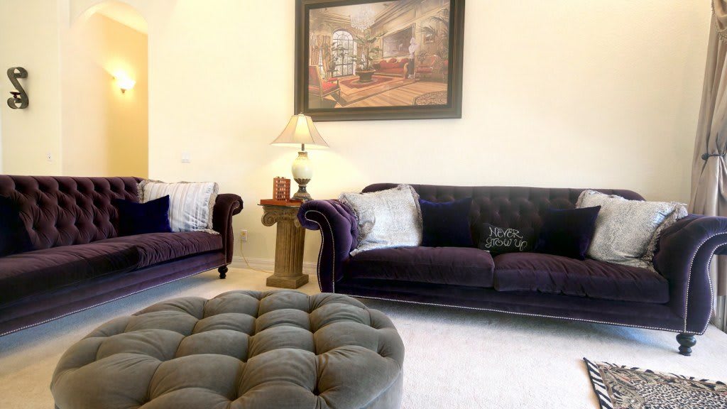 A cozy living room with plush sofas, a tufted ottoman, and elegant decor.