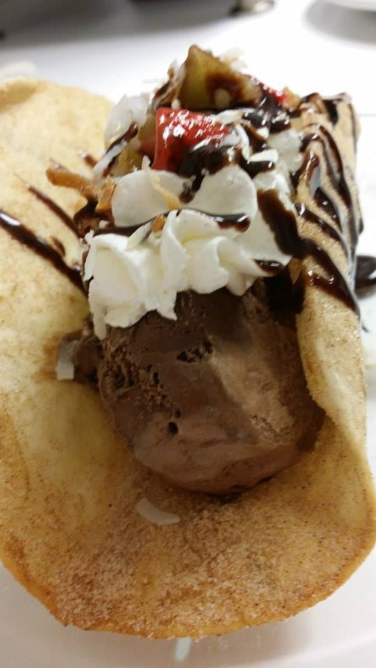 A delicious crepe filled with chocolate ice cream, topped with whipped cream and drizzled with chocolate sauce.