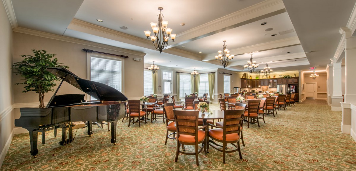 A spacious dining area with elegant chandeliers, a grand piano, and neatly arranged tables and chairs.