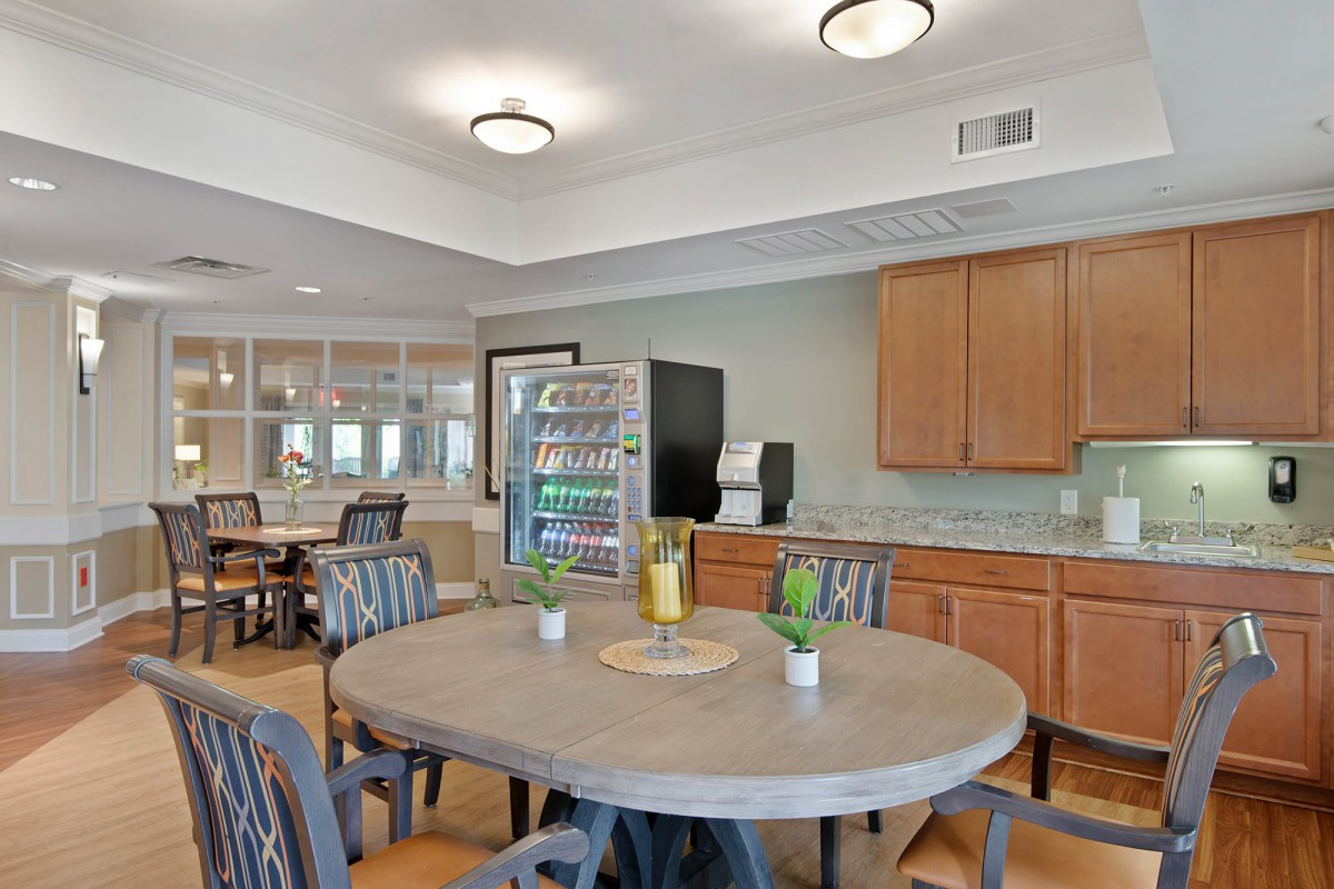 A cozy dining area with a round table, surrounded by chairs, featuring wooden cabinets and a vending machine.