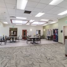 A modern cafeteria with tables, chairs, and vending machines in a spacious, well-lit area.