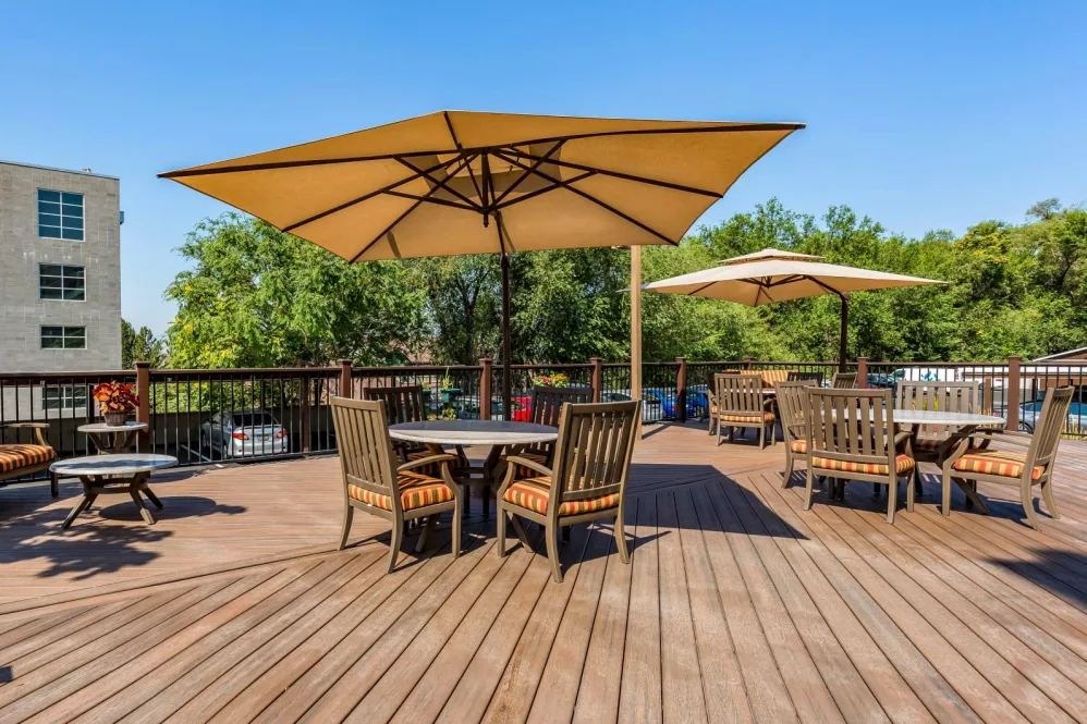 An outdoor patio deck featuring tables and chairs with large umbrellas on a sunny day.