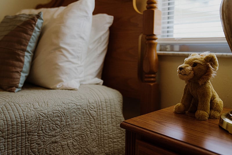 A cozy bedroom with a neatly made bed, a quilt, and a teddy bear on the nightstand.