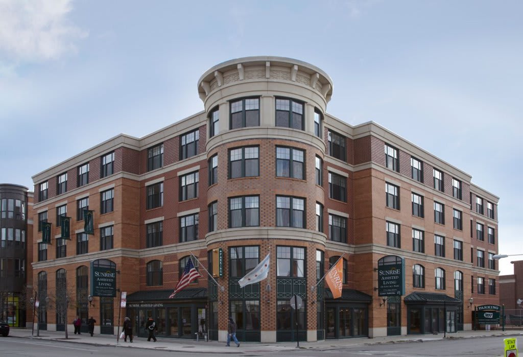 A modern, multi-story brick building situated at a street corner, featuring large windows and various flags displayed outside.