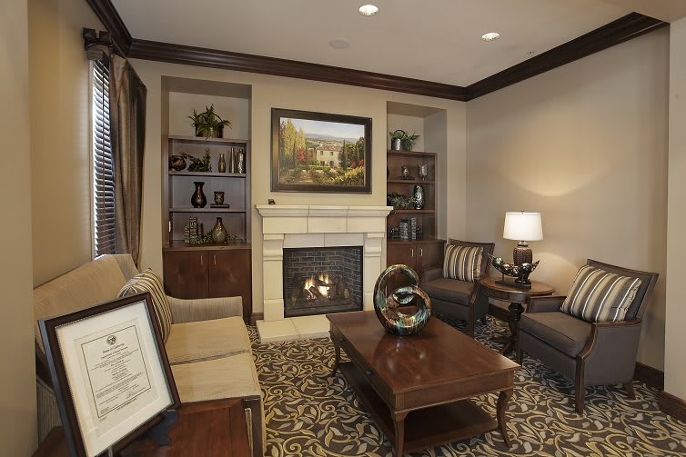 A cozy living room with a fireplace, surrounded by sofas and decorated with a coffee table, bookshelves, and a painting above the mantel.