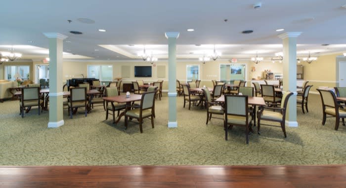 A spacious dining room with neatly arranged tables and chairs, featuring a carpeted floor and bright lighting.