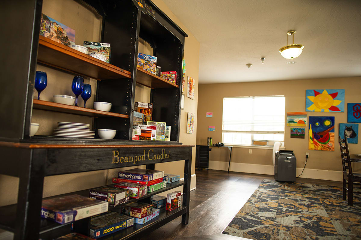 A cozy room with shelves filled with board games and kitchenware, illuminated by daylight through a large window.
