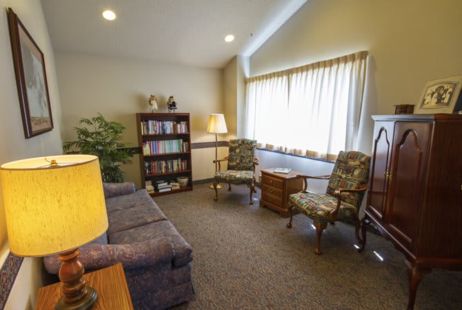 A cozy living room with a sofa, chairs, a bookshelf, and a window with curtains.