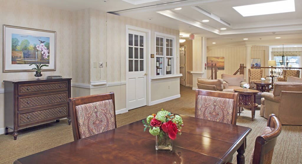 A cozy dining area with a wooden table and floral centerpiece, surrounded by comfortable chairs in a warmly lit room.