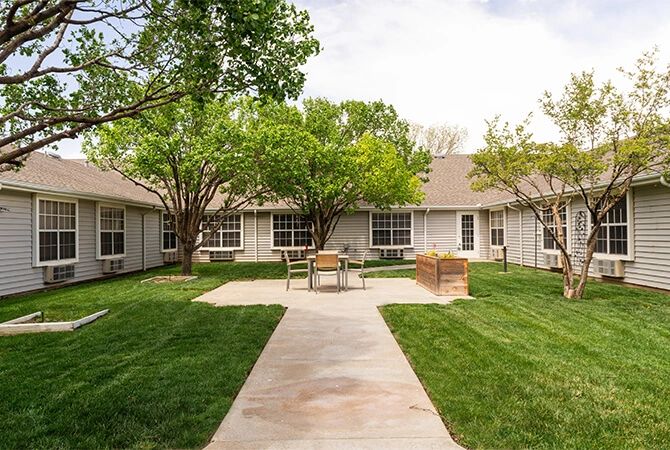 A peaceful courtyard with trees, grass, and benches surrounded by a building.