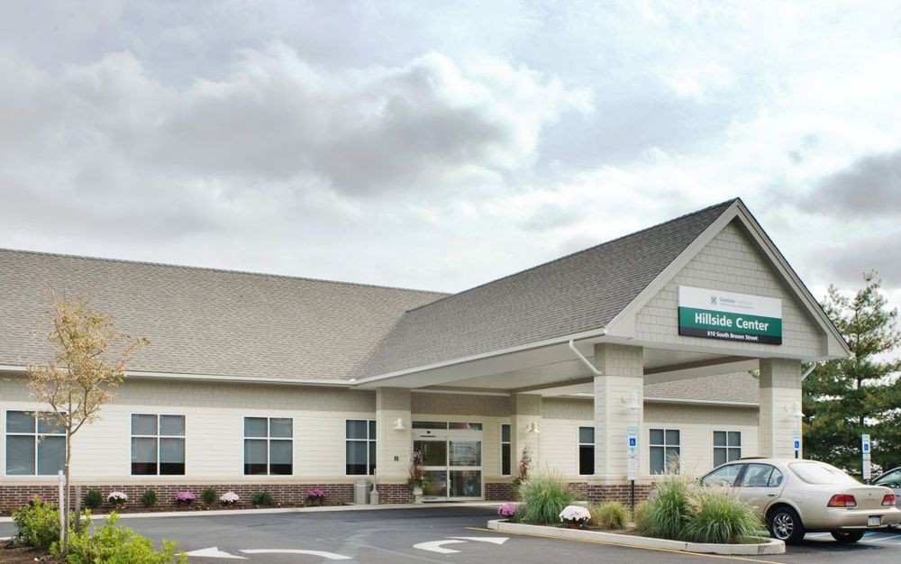 A healthcare clinic with a welcoming entrance and cloudy sky backdrop.