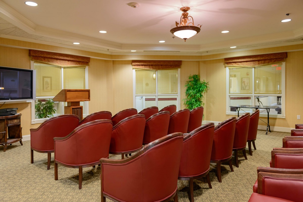 A well-arranged conference room with red chairs and a podium, ready for a presentation or meeting.