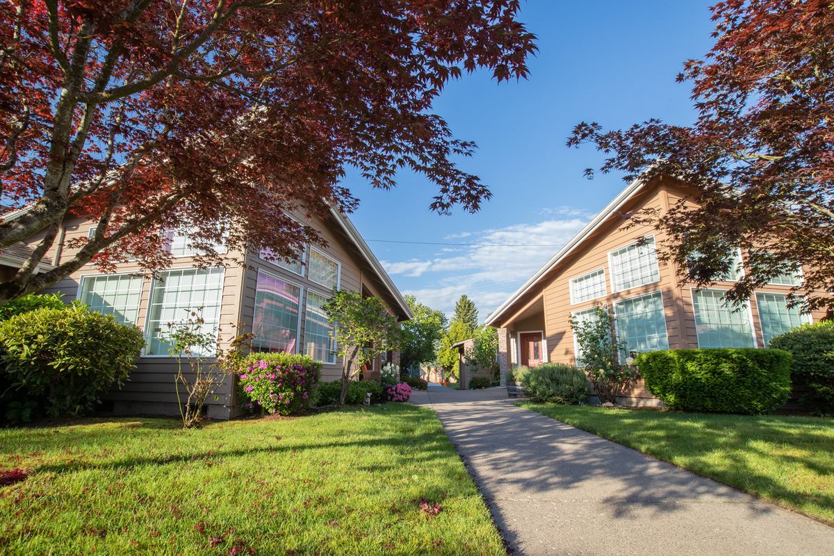 A sunny view of suburban residential buildings with a landscaped garden and pathway.