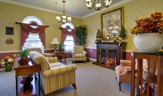 A cozy living room with traditional decor features a fireplace, armchairs, and chandeliers.