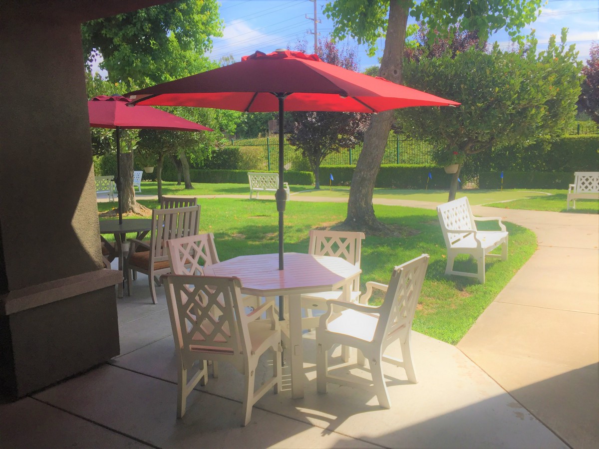 A sunny patio area with a table, chairs, and red umbrellas in a garden setting.