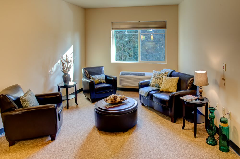 A cozy living room with comfortable armchairs and a round coffee table, illuminated by natural light from the window.