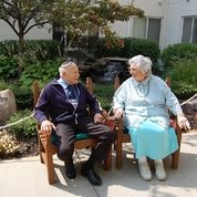 An elderly couple sitting together on benches in a garden.