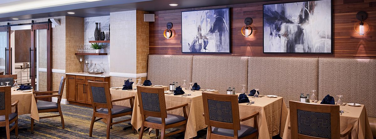 A cozy restaurant interior with elegantly set tables and artwork on the wall.