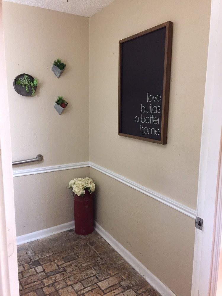 A small bathroom corner featuring a chalkboard, wall-mounted plants, and a vase with flowers.
