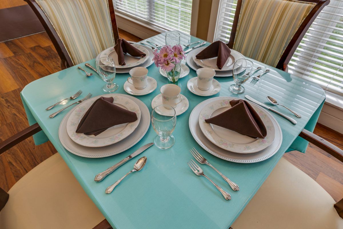 A formal dining table set with turquoise tablecloth and folded napkins.
