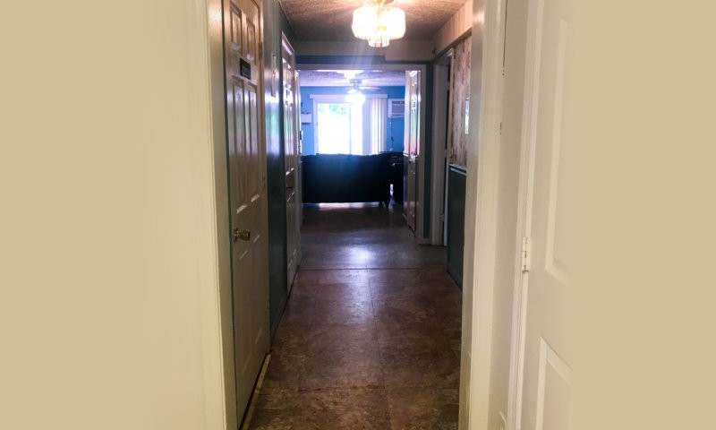 A hallway with a chandelier, leading to a brightly lit room.
