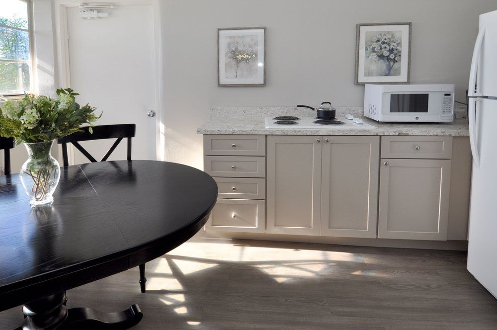 A minimalist kitchen with white cabinets, a microwave, and a black dining table.