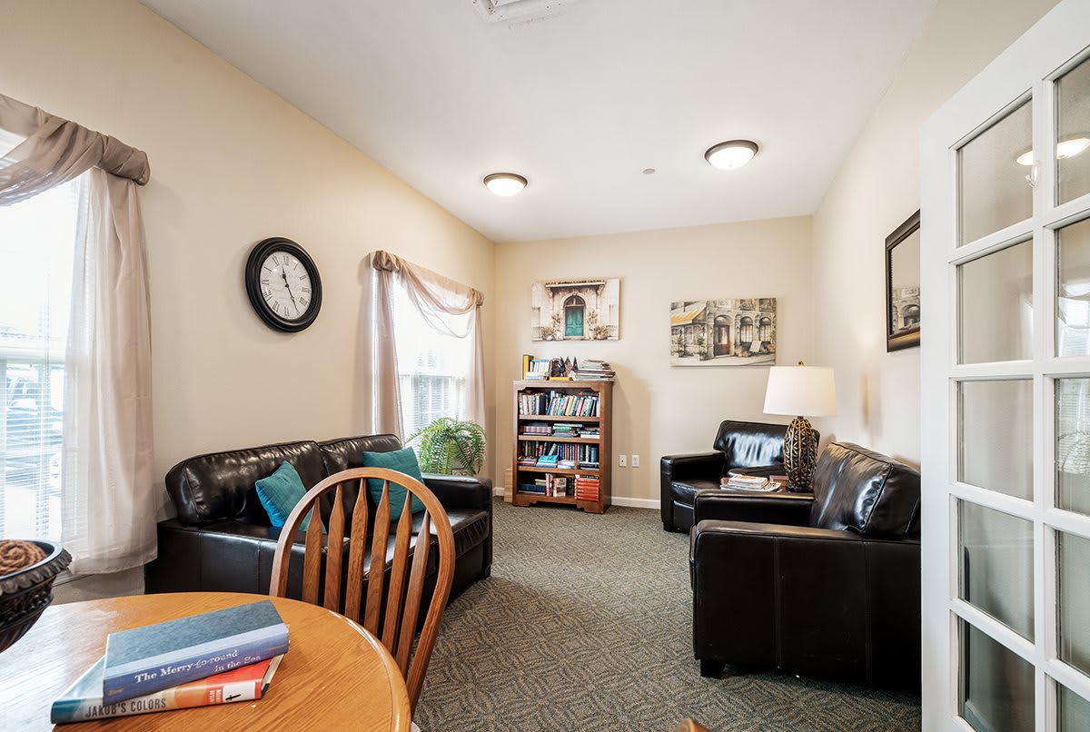A cozy living room featuring two sofas, a bookshelf, a table with chairs, and decorative elements such as a clock and wall art.