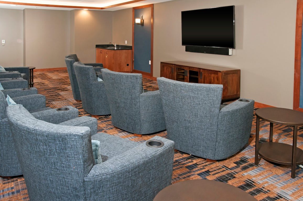 A cozy theater room with cushioned lounge chairs arranged in rows facing a large flat-screen TV.