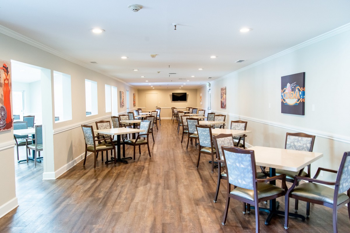 An empty dining room with wooden floors and arranged tables and chairs.