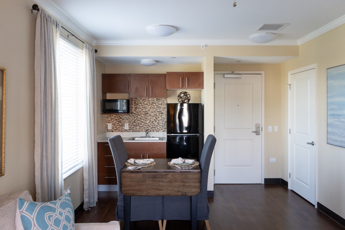 A modern kitchen and dining area in an apartment, featuring a table set for four, with a fridge and microwave in the background.