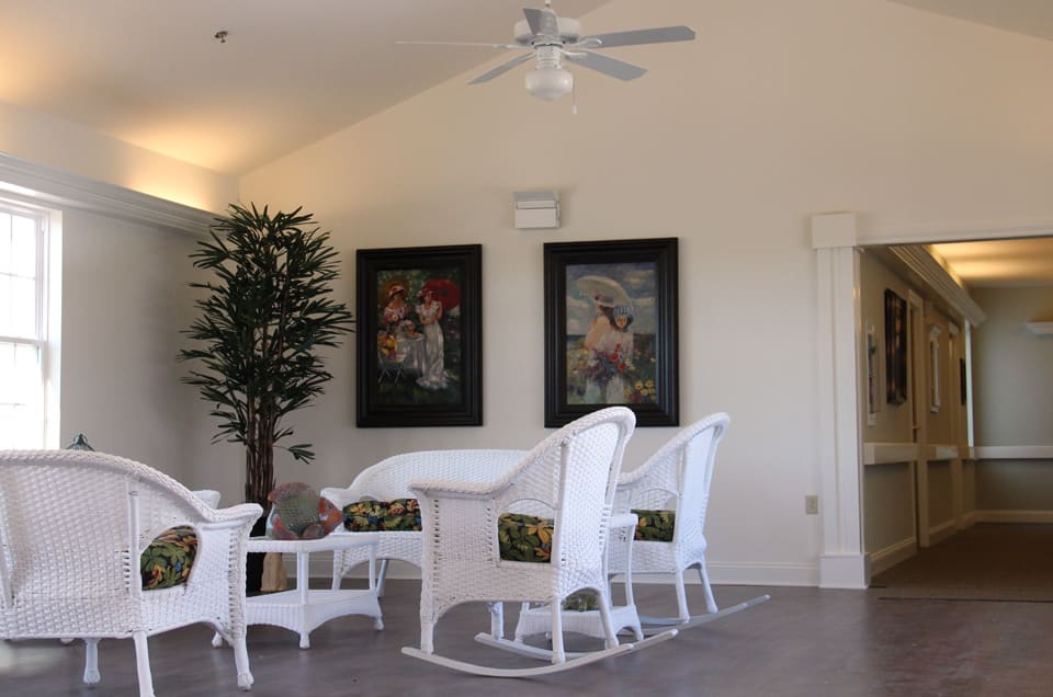 A cozy living room featuring white wicker furniture, framed artwork, and a potted plant.