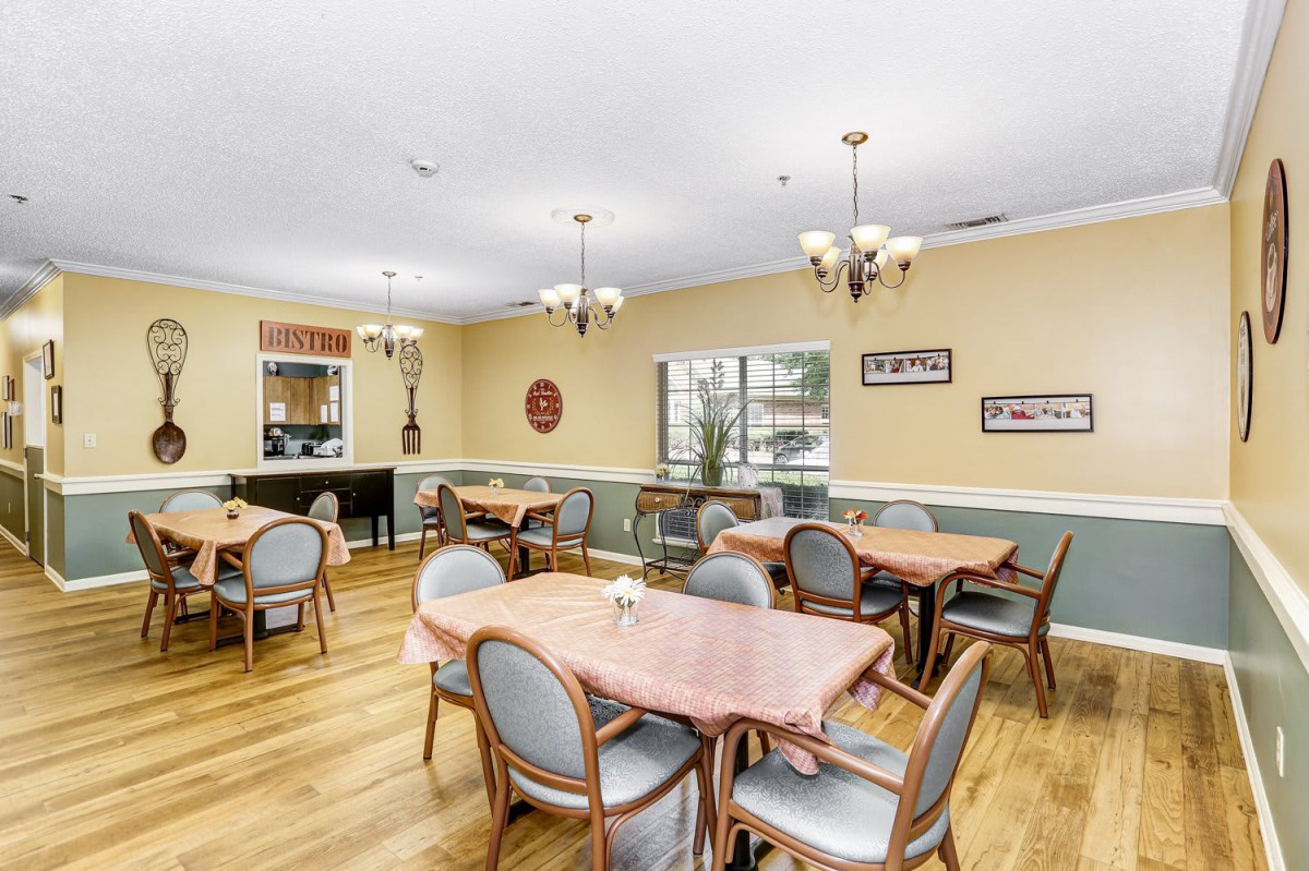A cozy dining room with multiple tables and chairs, featuring chandeliers and wooden flooring.