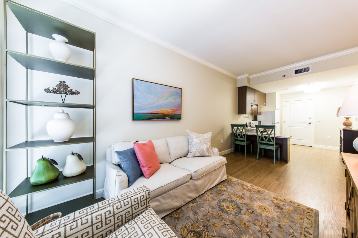 A cozy living room with a modern sofa, decorated with colorful pillows, adjacent to a dining area and stylish shelving.
