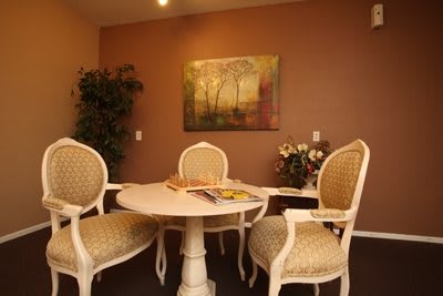 A cozy dining area with elegant chairs around a round table, adorned by a wall painting and indoor plant.