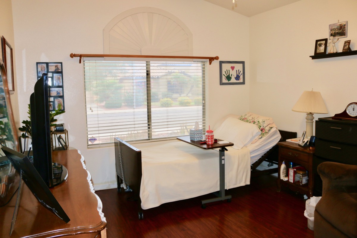 A cozy bedroom featuring a hospital bed near a large window with blinds, offering a view of the outside.