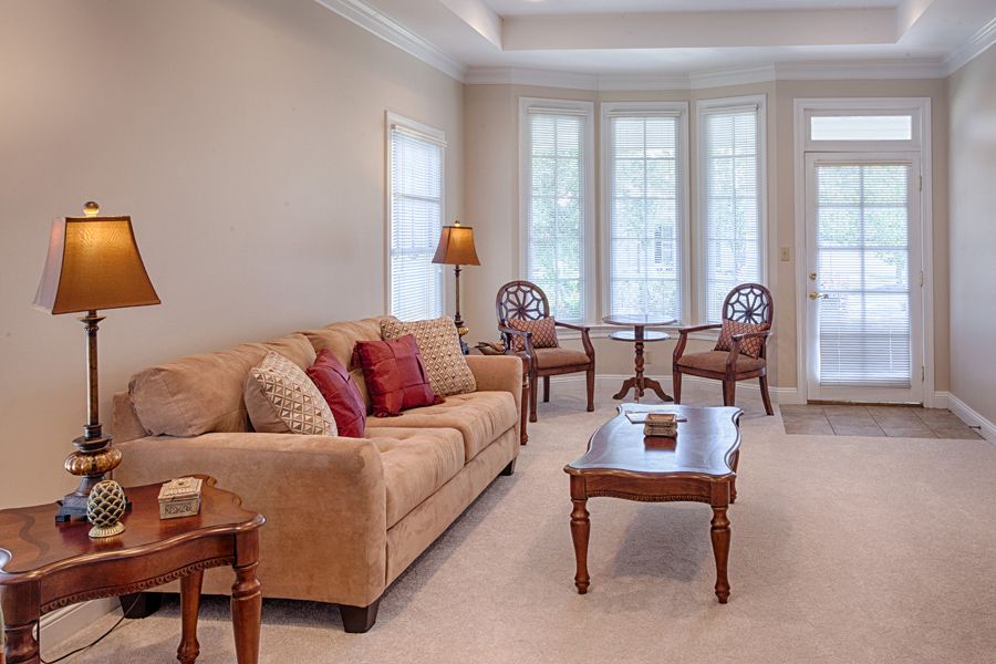 A cozy living room with a sofa, coffee table, and natural light from tall windows.