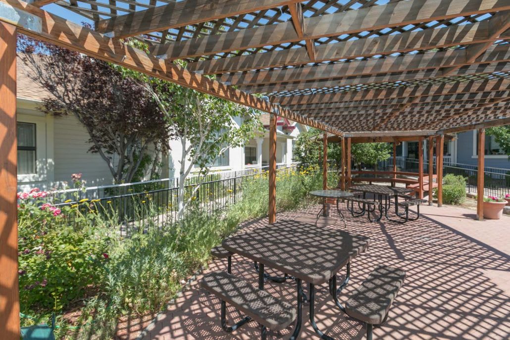 An outdoor seating area under a pergola, surrounded by lush greenery.
