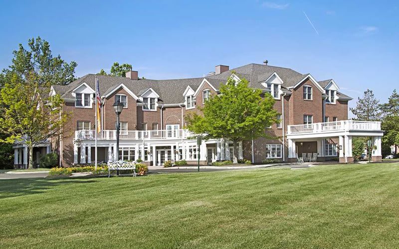 A large residential building with a well-maintained lawn and trees under a clear sky.