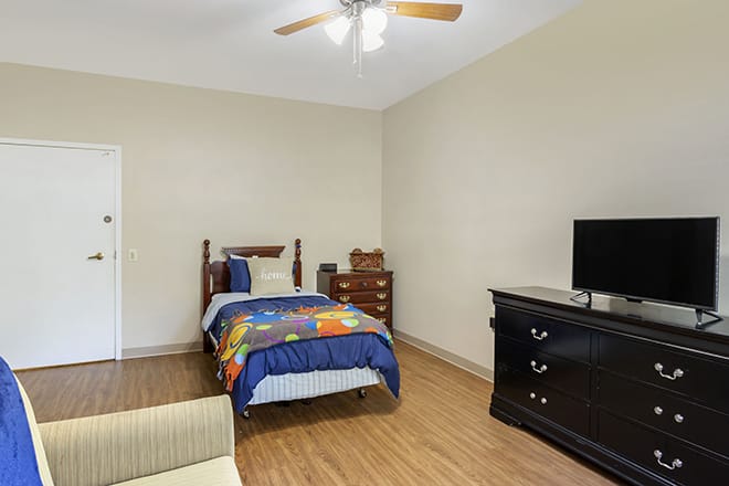 A minimalist bedroom with a single bed, television, and dresser on a wooden floor.