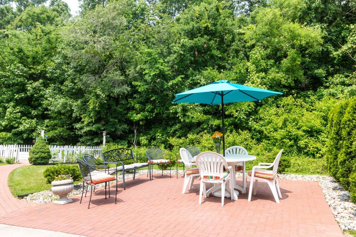 A sunny outdoor patio with a table, chairs, and an umbrella surrounded by lush greenery.
