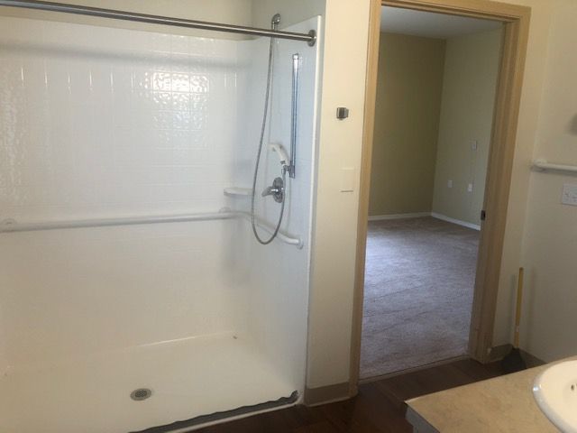 A minimalist bathroom with a walk-in shower and an adjoining empty room.