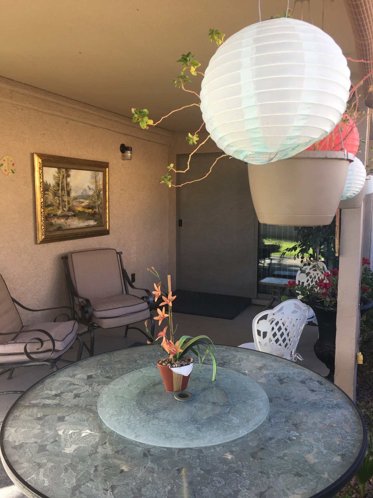 A cozy patio with a glass table, cushioned chairs, and hanging plants.