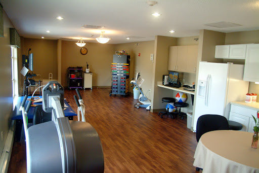 A spacious and well-lit room featuring exercise equipment and a kitchenette area.