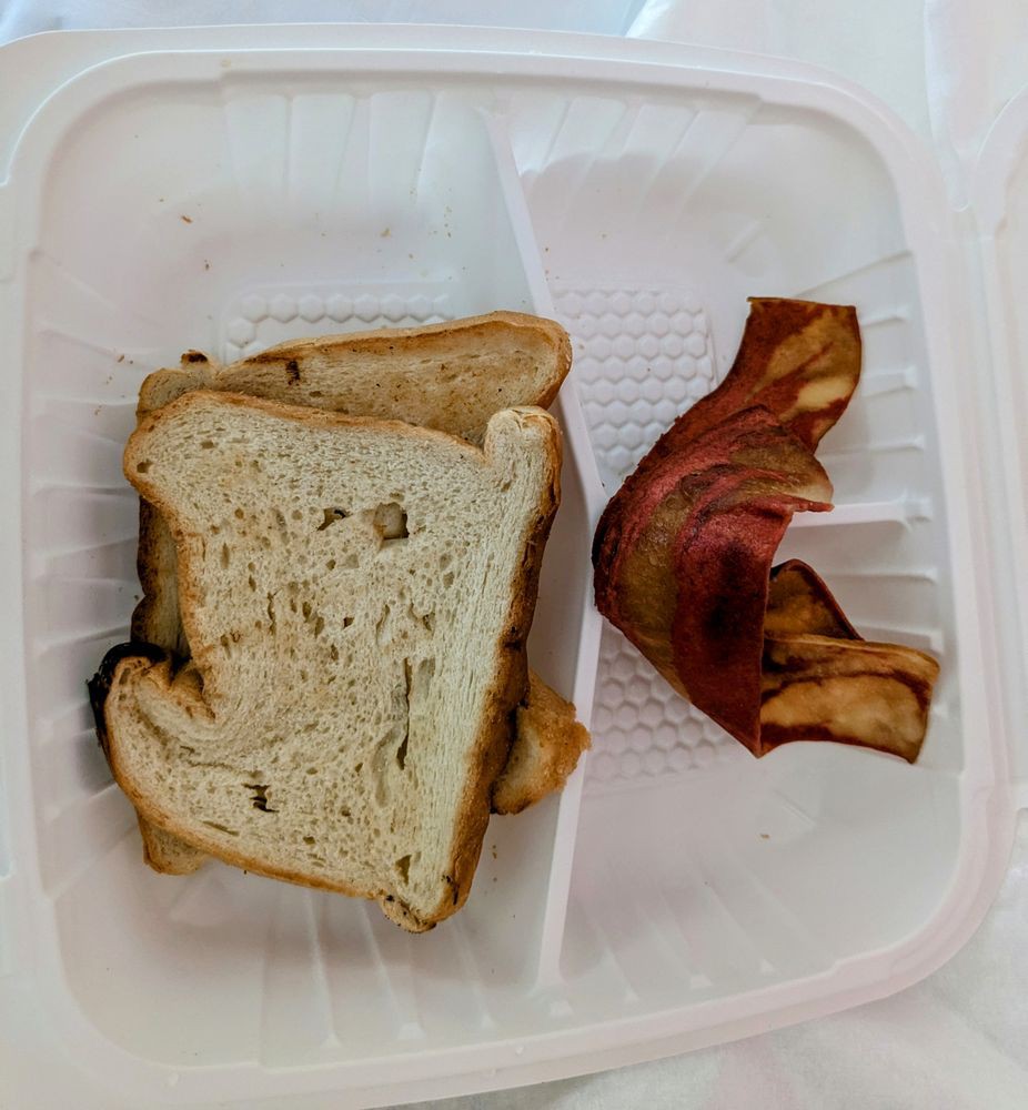 A simple meal with a sandwich and bacon in a plastic container.