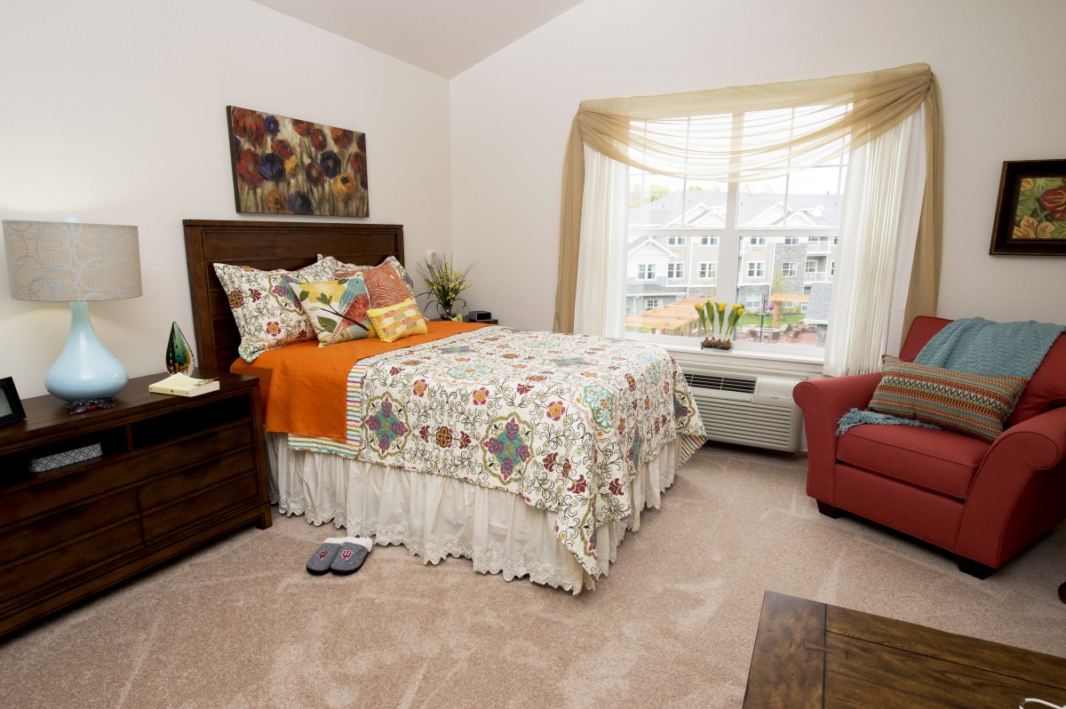 A cozy bedroom with a neatly made bed, large window, and warm decor.