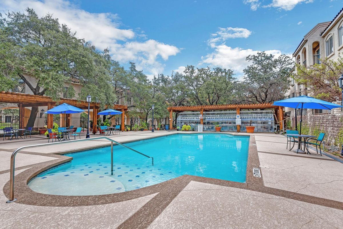 A serene outdoor swimming pool surrounded by trees with lounge chairs and sun umbrellas.