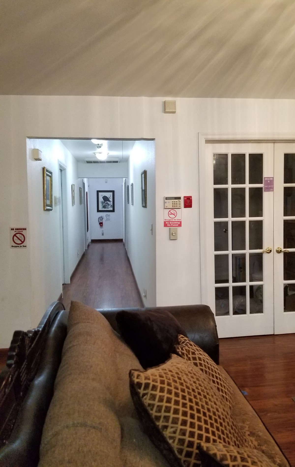 A cozy living room with a couch and French doors leading into a well-lit hallway adorned with framed pictures.