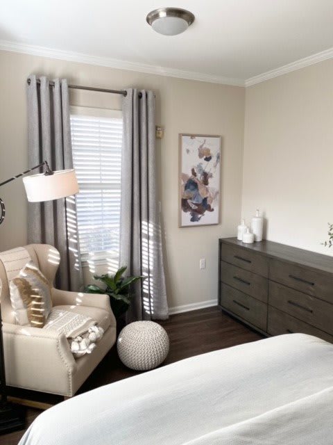 A cozy bedroom with a chair, lamp, and dresser alongside decorative elements.