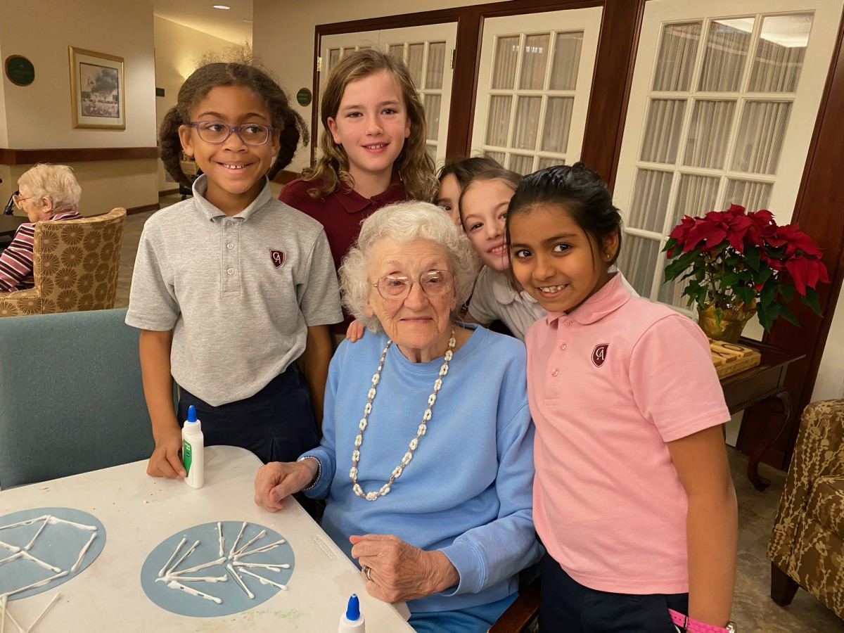 A group of children smiling and posing with an elderly woman indoors.